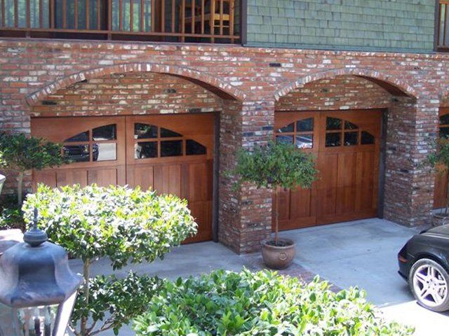 Two arched wood carriage doors on a brick home
